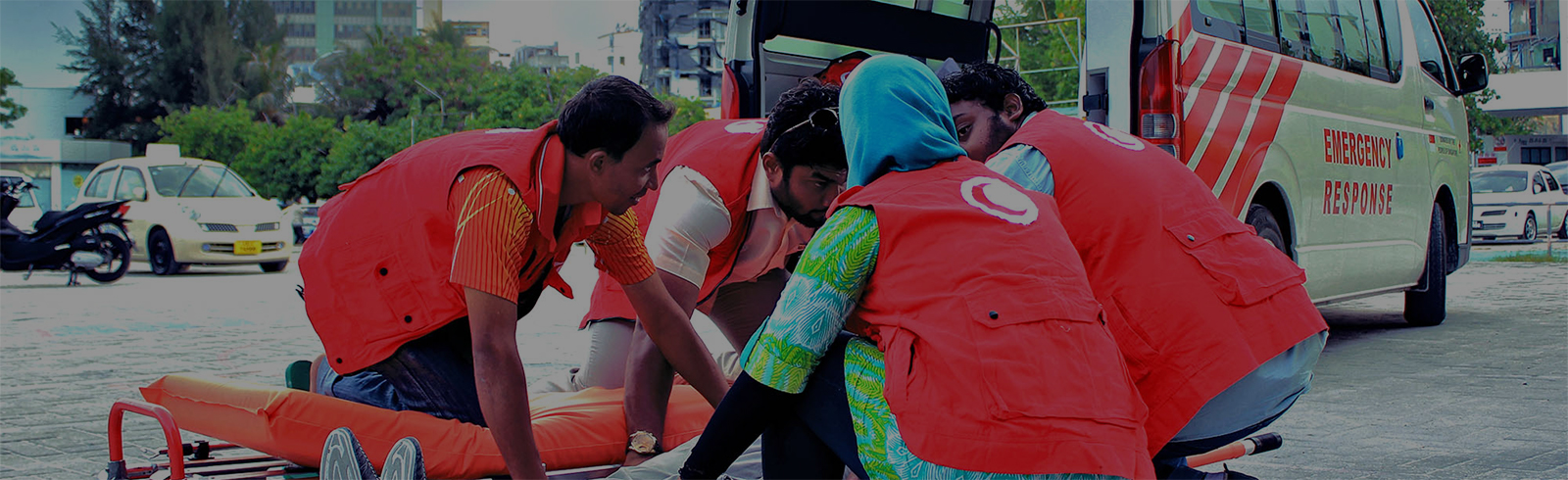 An image of red crescent volunteers assisting an injured person on a stretcher near a red crescent ambulance